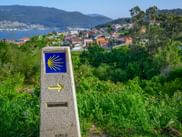 Steinmarkierung mit gelber Jakobsmuschel auf blauem Grund am Portugiesischen Jakobsweg mit Blick auf Vigo, Küstenstadt und Bucht.