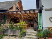 Holzpergola-überdachte Restaurantterrasse in Bled mit Lichterketten, Holztischen, Pflanzgefäßen und einer Kreidetafel am Eingang.