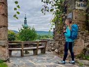 Female hiker with blue backpack at stone archway in Stein an der Donau, Wachau. Church tower and hills visible in background.