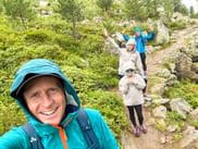 Selfie of a smiling Thomas in rain gear with three family members behind him on a rocky mountain trail, surrounded by green vegetation.