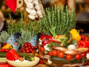 Frisches Gemüse in einer Glasschüssel wie beispielsweise Zucchini, Paprika, Tomaten, Zwiebel, Knoblauch, Rosmarin im Hintergrund