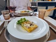 Plate with aubergine lasagne and arugula salad, served with red wine in Barolo, Piedmont. A second plate is visible in the background.