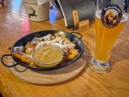 Kaiserschmarrn in schwarzer Pfanne mit Puderzucker bestreut, serviert mit Apfelmus und einem Glas Franziskaner Weißbier auf Holztisch.