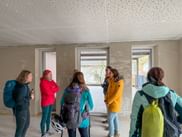 Group of six people in colorful outdoor jackets standing in an unfinished room with concrete walls and ceiling during Eurofun company trip.