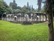 Steinruinen mit Bogengängen im Parco della Valletta, Gardone, umgeben von grünem Rasen und Zypressen in der Nähe des Gardasees.