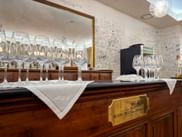 Wine tasting room with rows of empty wine glasses on wooden cabinet. Gold plaque reads 'Marchesi di Barolo'. White walls with signatures.