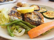 Plate with two grilled fish fillets, a slice of lemon, grilled courgettes, salad and boiled carrots and sugar snaps