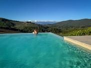 Frau in türkisfarbenem Infinity-Pool mit Blick auf toskanische Hügel bei Greve in Chianti. Weinberge und grüne Hügel unter blauem Himmel.