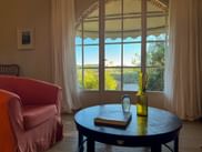 Elegantes Hotelzimmer im Hotel Pietra del Cabreo mit Bogenfenster und Blick auf toskanische Hügel, rosa Sessel und rundem Tisch mit Dekoration.