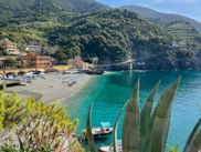 Scenic bay of Monterosso al Mare with turquoise water, beach, colorful buildings, and green terraced hills in Cinque Terre, Liguria.