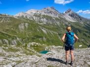 Wanderin mit blauem Rucksack blickt auf den Knoppigsee in den Allgäuer Alpen, mit felsigen Gipfeln und grünen Almwiesen.