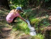 Child in pink shirt and cap crouching beside a small stream on the Waalweg trail near Mals-Schluderns, South Tyrol, touching the flowing water.