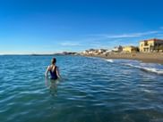Frau im ruhigen blauen Meer am Strand von Cecina Mare in der Toskana. Küstengebäude und klarer Himmel im Hintergrund.