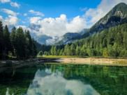Kristallklarer Jasna See mit smaragdgrünem Wasser, das Berge und Wälder spiegelt. Dichte Nadelwälder umgeben den See in den Julischen Alpen.