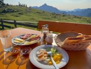 Breakfast table at Postalm with bread, cheese, cold cuts, boiled eggs, and jam. Alpine meadows and mountains visible in background.