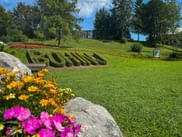 Gepflegter Rasen mit 'BOHINJ'-Schriftzug aus geschnittenen Hecken, umgeben von bunten Blumenbeeten und Bäumen, Bohinjer See im Hintergrund.
