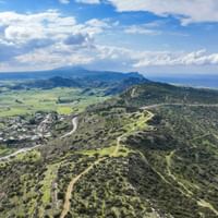 Aerial view of rolling hills and green valleys in Cyprus near Famagusta, with winding dirt roads crossing the landscape under a cloudy sky.