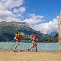 Zwei Wanderinen am Ufer des Reschensees bestaunen den versunkenen Kirchturm