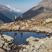 Reflection of two hikers in a mountain lake with panorama