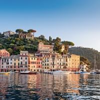 Portofino harbor with colorful pastel buildings along the waterfront, boats and yachts moored in calm water, hillside villas above.