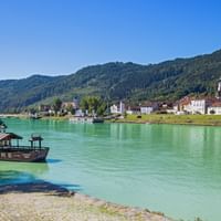 Traditional wooden ferry on turquoise Danube River near Engelhartszell with colorful buildings and forested hills in background under blue sky.