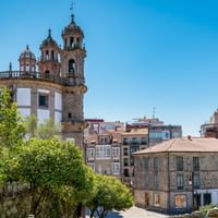 La Peregrina Kirche mit markanten Glockentürmen in Pontevedra, umgeben von Wohngebäuden und grünen Bäumen unter blauem Himmel.