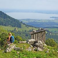 Two hikers on an alpine meadow with a view of the Friedenrath and Lake Chiemsee