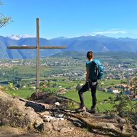 Hiker at a summit cross with a view of the Adige valley
