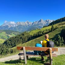 Hiker on a bench in front of a mountain panorama