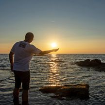 Man stands on the beach and holds his right hand to the setting sun, sunset, sea