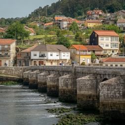 Alte Steinbrücke über einen Fluss in Ponte Sampaio mit traditionellen Häusern und orangefarbenen Ziegeldächern am Hang im Hintergrund.