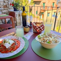 Zwei Salate auf einem Terrassentisch in Panzano: Burrata mit Tomaten und ein gemischter Salat mit Birnen und Walnüssen. Olivenöl und Limonade runden das Essen ab.