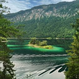 Malerischer Blick auf den Eibsee mit kristallklarem türkisfarbenem Wasser, kleiner bewaldeter Insel und bewaldeten Bergen.