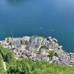 Aerial view of Hallstatt village with church spire, traditional houses, and wooden piers on blue lake water, surrounded by green forest.