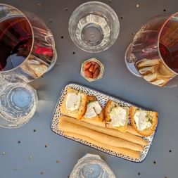 Overhead view of wine tasting setup with two glasses of red wine, water glasses, and a plate of bruschetta with breadsticks on a gray table.
