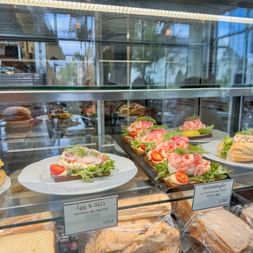 Vitrine mit Krabbenbroten auf weißen Tellern, garniert mit Salat und Tomate. Etiketten zeigen schwedische Namen in Kungsbacka.