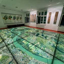 Large floor map of Wachau wine region near Krems displayed in museum room with vineyard illustrations on walls and decorative panels between windows.