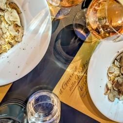 Two plates of fresh pasta topped with shaved truffles and black pepper, served with a bottle of rosé wine and glasses on a dark table.
