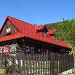 Landestypisches dunkelbraunes Holzhaus mit weißen Mustern und rotem Ziegeldach in der Gemeinde Cicmany