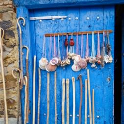 Hölzerne Pilgerstäbe und Jakobsmuscheln hängen an einer verwitterten blauen Holztür neben einer Steinmauer am portugiesischen Jakobsweg.