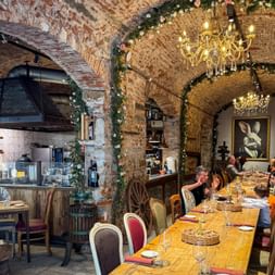 Rustikales Restaurant in Florenz mit Ziegelgewölbe, Kronleuchtern und Gästen an langen Tischen. Offene Küche unter Rundbogen sichtbar.