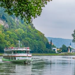 White excursion boat on the Danube River near Kelheim with forested cliffs and a village with church towers in the background.