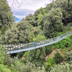 Ponte Tibetano Crero suspension bridge with colorful prayer flags spanning a forested valley near Lake Garda. Hikers crossing the bridge.