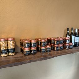 Wooden shelf displaying local products from Cravanzana: hazelnuts in glass jars, black jars with copper lids, and wine bottles against a beige wall.