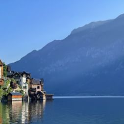 Traditionelle bunte Häuser von Hallstatt entlang des ruhigen Seeufers mit steilen Bergen im Hintergrund unter klarem blauen Himmel.