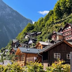 Traditional wooden and painted houses in Hallstatt village nestled against a forested mountainside under blue sky in the Salzkammergut region.