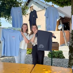 Two smiling women holding up Eurohike branded t-shirts at an outdoor event with more shirts hanging on a clothesline behind them.