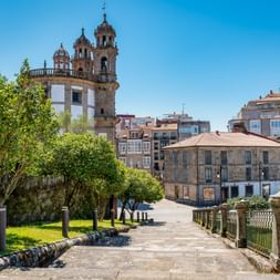 Steinweg zur La Peregrina Kirche mit markanten Glockentürmen in Pontevedra, gesäumt von grünen Bäumen und historischen Gebäuden.