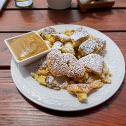 Traditional Kaiserschmarrn dusted with powdered sugar on a white plate, served with applesauce in a small bowl on a wooden table.