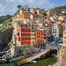 Colorful houses stacked on cliffs in Riomaggiore, Cinque Terre. Buildings in yellow, pink, orange, and red overlook a small harbor with boats.